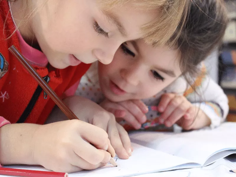 Two people writing on a piece of paper.